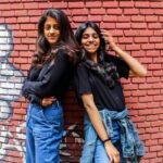 Two women in casual outfits posing confidently against a graffiti brick wall.